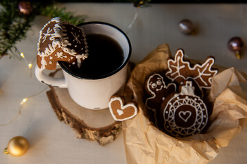 Warm mug with hot coffee or tea and a gingerbread cookie on the rim, next to a basket filled with various decorated gingerbread cookies, setting a festive winter holiday scene