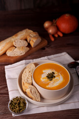 warm and inviting autumn scene with creamy pumpkin soup garnished with seeds and cream, accompanied by crusty french baguette slices on a wooden table with fresh vegetables in the background