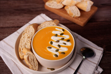 creamy pumpkin soup garnished with cream and pumpkin seeds served with artisan bread on a rustic wooden table setting, creating a cozy and inviting autumn meal scene, french, aesthetic, presentation
