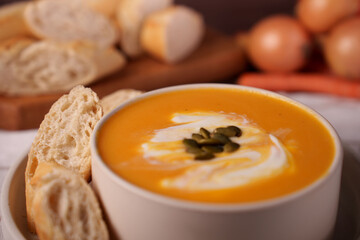 warm carrot soup with sour cream swirl and pumpkin seeds, accompanied by fresh slices of bread, set in a cozy dining setting with a rustic ambiance, setting, ingredients, vegetables, appetizer