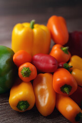 a vibrant assortment of fresh, colorful bell peppers and chilis showcasing varying shades of yellow, orange, red, and green, arranged on a rustic wooden surface, emphasizing their natural beauty