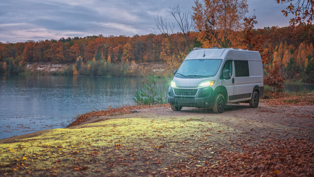panoramic view in twilight to white camper van on lake coast in rainy evening with copy space