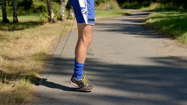 man retrieves jump rope, man leans down to grasp jump rope on shaded trail during cooldown walk, white man softly bends to retrieve jump rope along shaded summer trail during relaxed cooldown walk