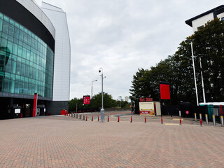 Fototapeta premium Manchester city center modern building with glass facade, plaza, red signage and street bollards