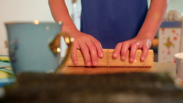 Preparing sushi on bamboo mat at home, Woman expertly rolling sushi with rice and seaweed on kitchen