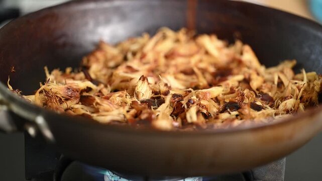 Close-up of shredded Lion's Mane mushrooms being stirred with sticky sauce in a hot pan. Healthy, nutritious, vegan meat alternative.
