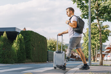 Man with a prosthetic leg walks rolling his trolley suitcase along the street. Disability, mobility, and travel concept.