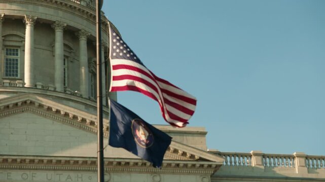 United States flag with Utah state flag waving in slow motion at the Utah State Capitol building