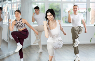 Fototapeta premium Positive woman and man engaged in dancing in group practices energetic swing in a dance studio