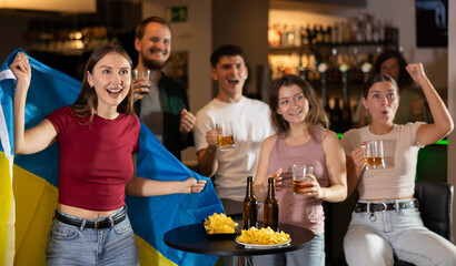 Group of friends fans watching match cheering with Ukrainian flag in bar