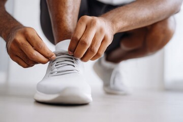 African American man ties shoelace on pristine white running shoe, preparing for daily exercise routine.