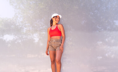 Young woman posing outdoors, looking right, wearing a red sports bra and hat