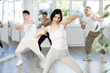 Fototapeta premium Girl conducts lesson for group of young people, demonstrates basic movements for performing locking dance, teaches modern dance culture directions