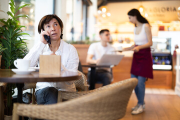 Elderly woman talking on mobile phone and drinking coffee in cafe