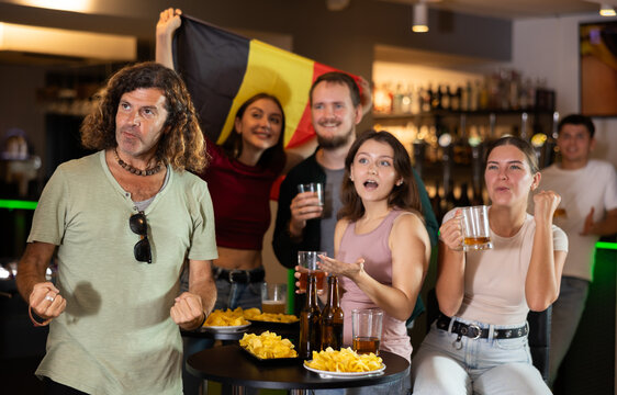 Happy girls adm men with Belgian flag celebrates the victory of her favorite team in a beer bar