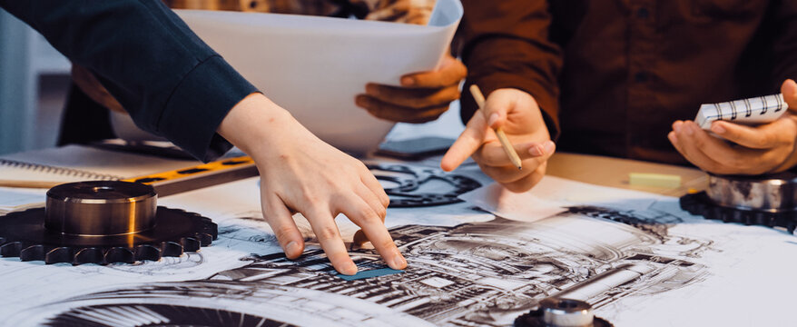 A group of engineers collaborates on technical drawings, analyzing components and specifications. They focus on creativity and precision in a collaborative workspace. SACTR - Powered by Adobe