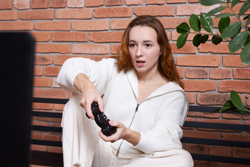 A middle-aged man gamer holds a gamepad and plays an online game on a computer.