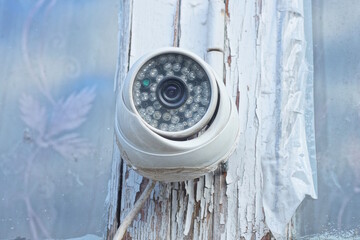 A single white webcam hangs on the board of an old window frame on a summer street
