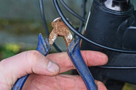A man holds a rusty wire cutter in one hand, which he uses to cut off a wire on a summer street