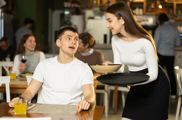 Smiling female waitress brings ordered food to european guy. Restaurant customer asks the waitress about the dishes of the day, talks about his food preferences and allergies