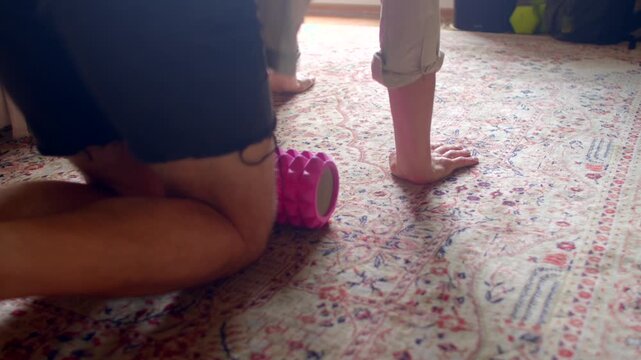 Stretching before running, Performing dynamic stretching by rolling hamstring on pink roller in living room