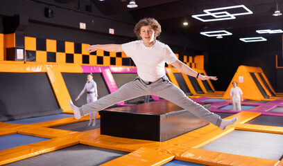 Dynamic teenage boy wearing sport clothes high jumping in trampoline arena