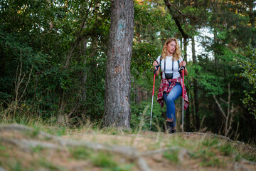 Obraz premium Woman hiking in forest using trekking poles