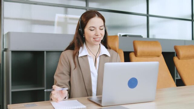 Consultant assists clients in a modern office using a laptop and headphones during a business call in a collaborative coworking space - Powered by Adobe