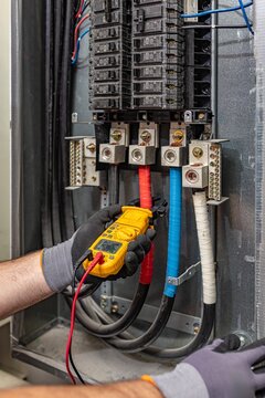 Electrician measuring current load on three-phase electrical panel using clamp meter, Florida, USA