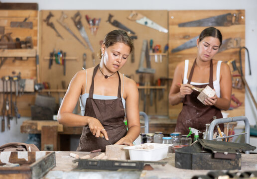 Girl is busy in carpentry workshop. Process wooden billet, sand it, applies pattern with cutter. Related stages of working with devices tools. In workshop girl stand with work gloves in hands