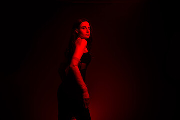 Young elegant woman in red lighting setting posing for stylish photoshoot with an aura of sensuality and glamour