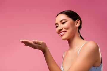 Portrait of a stunning woman with radiant makeup and styled hair against a pink background
