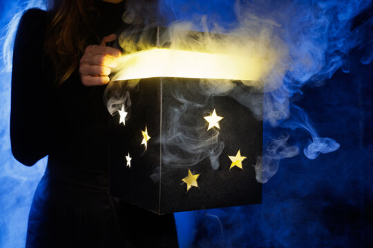 Opening glowing magic box with smoke and star cutouts on blue background