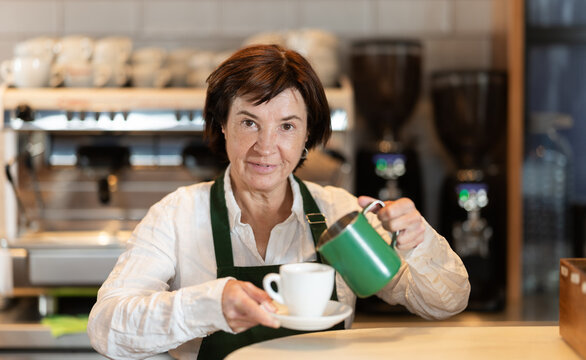 Elderly woman barista pouring freshly brewed coffee into cup in cafe