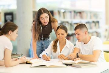 Group of student sits at table in library and studies, reads books and takes notes, makes summary,...