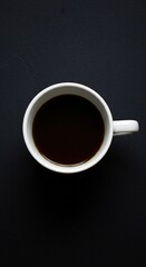 A top-down view of a white coffee cup filled with dark coffee, placed on a textured black surface.