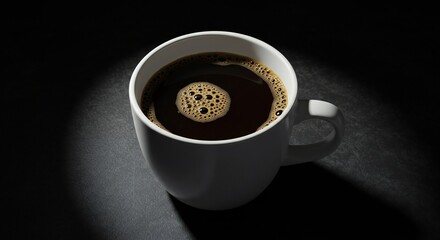 A white coffee cup filled with dark coffee, featuring a frothy surface with bubbles. The scene is set against a dark background, creating a stark contrast.