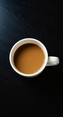A top-down view of a white coffee cup filled with brown coffee, placed on a dark wooden surface.