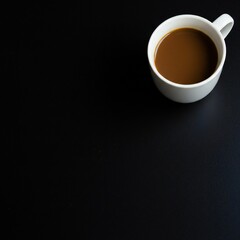 A white coffee cup filled with brown coffee sits on a black surface. The composition highlights the simplicity and elegance of the scene.