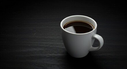 A white ceramic coffee cup filled with dark coffee sits on a textured black surface. The scene is minimalistic and focuses on the cup as the main subject.