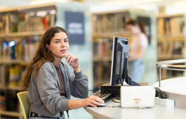 Female student is thoughtfully sitting near the computer monitor, she is preparing for exams in the...