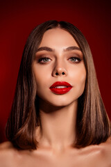 Portrait of a confident young woman with bold red lipstick and sleek brown hair against a rich red background