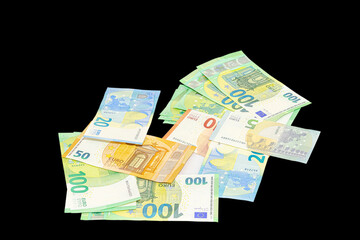 Pile of assorted euro banknotes including one hundred, fifty, twenty, ten and five euro notes scattered on a plain black background, tilted view, studio shot close-up macrophotography..