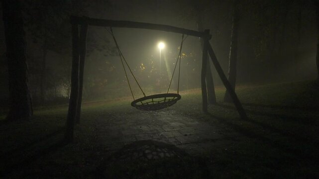 Cinematic 4K shot of empty swing moving at night under streetlight