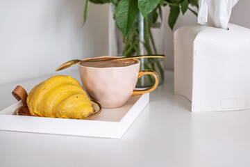 Fluffy croissant with yellow decoration sits on a white tray beside a pink cup, creating a delightful breakfast scene with inviting textures and warm ambiance