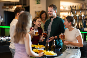 Happy mens and womens drinking beer and eating crisps, laughing and spending time together in a bar