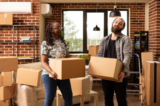Cheerful african american woman and caucasian man stand with moving boxes in new brick wall apartment. Couple posing on relocation day, representing lifestyle, partnership and new beginnings.