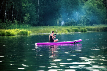 A woman sup surfing paddling on a boat on a river on sunny day.