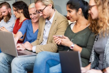 Group of diverse people sitting together, using laptops and phones, collaborating and working in a casual setting, focused on technology and teamwork. Diverse team of people working on laptops.