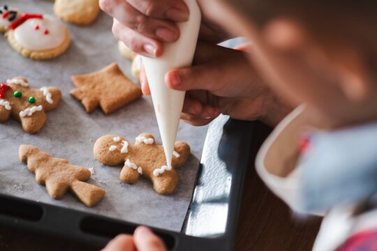 Child decorating gingerbread cookies with icing. Hands carefully icing cookies. Holiday baking, gingerbread, and icing. Close-up of festive cookie decorating. Child decorating gingerbread man cookie.
